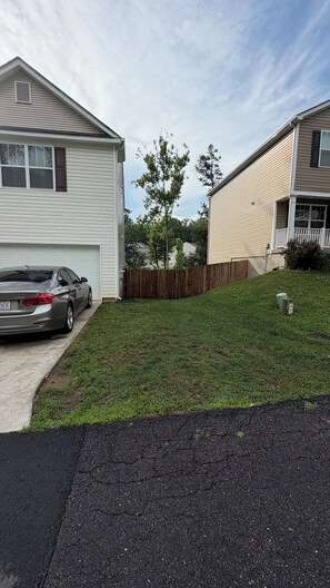 A residential driveway with a parked car, a wooden fence, and a grassy yard. - Cozy private space with an outdoor patio, 10 minutes from downtown Asheville (Candler)