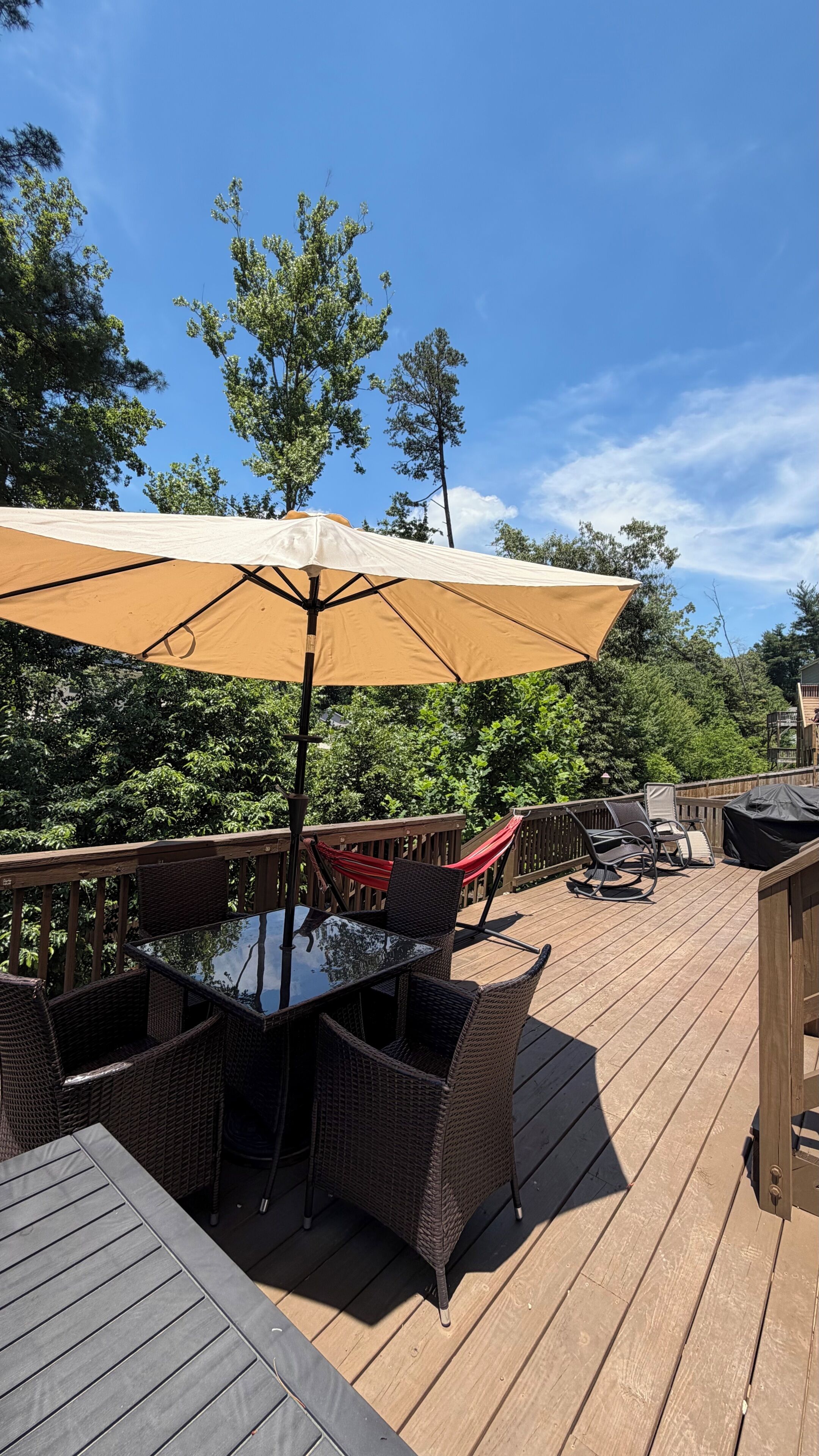 A wooden deck with a dining table and chairs, a large umbrella, and a hammock.