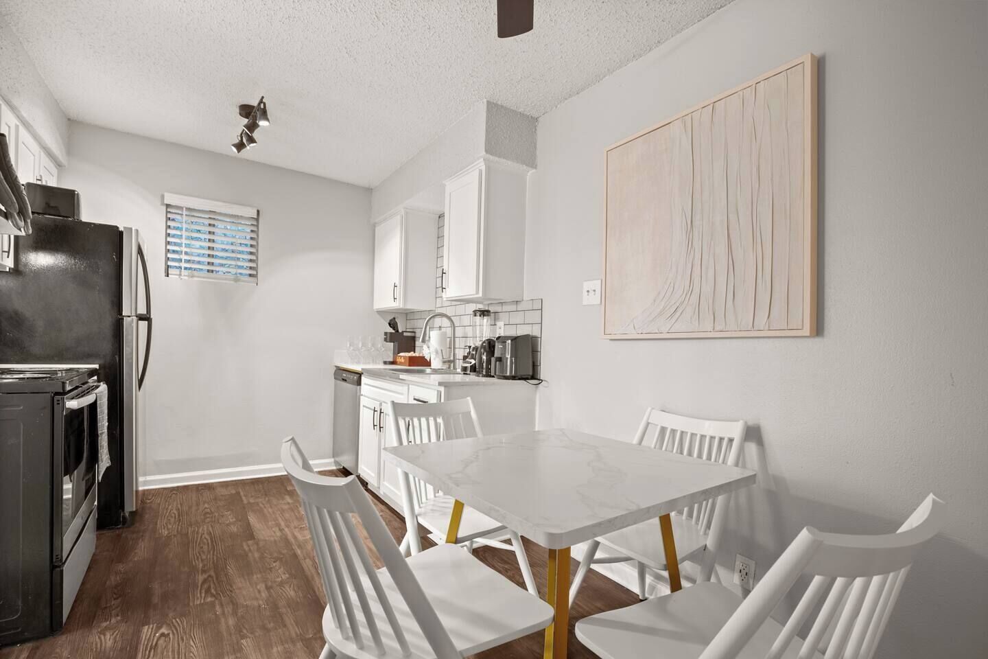 A modern kitchen with white cabinetry, a marble countertop, and a dining area with white chairs and a marble table.