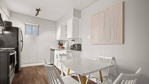 A modern kitchen with white cabinetry, a marble countertop, and a dining area with white chairs and a marble table. - Zilker Park Studio | Near Barton Springs &Downtown (Austin)