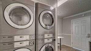 A laundry room with four stacked front-loading washers and dryers, a small white sink, and a door to the right. - Zilker Park Studio | Near Barton Springs &Downtown (Austin)