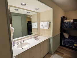 Un baño con lavamanos doble, un espejo grande y una cama con colcha azul estampada.