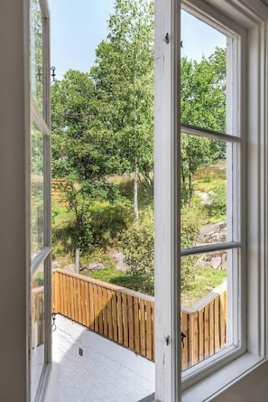 A room with a large window overlooking a garden with trees and a wooden deck.