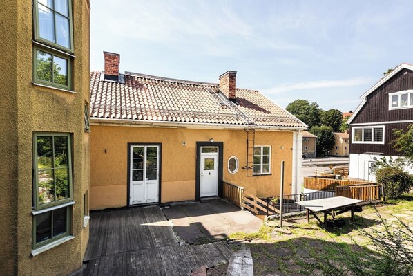 A two-story house with a tiled roof, a wooden deck, and a small outdoor seating area.