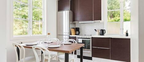 A modern kitchen with a dining area, large windows, and dark cabinetry.