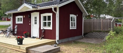 A small red cabin with a deck, a chimney, and a fenced yard.