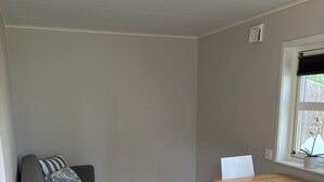 Une pièce avec un canapé gris, une table à manger en bois et une fenêtre avec des stores.