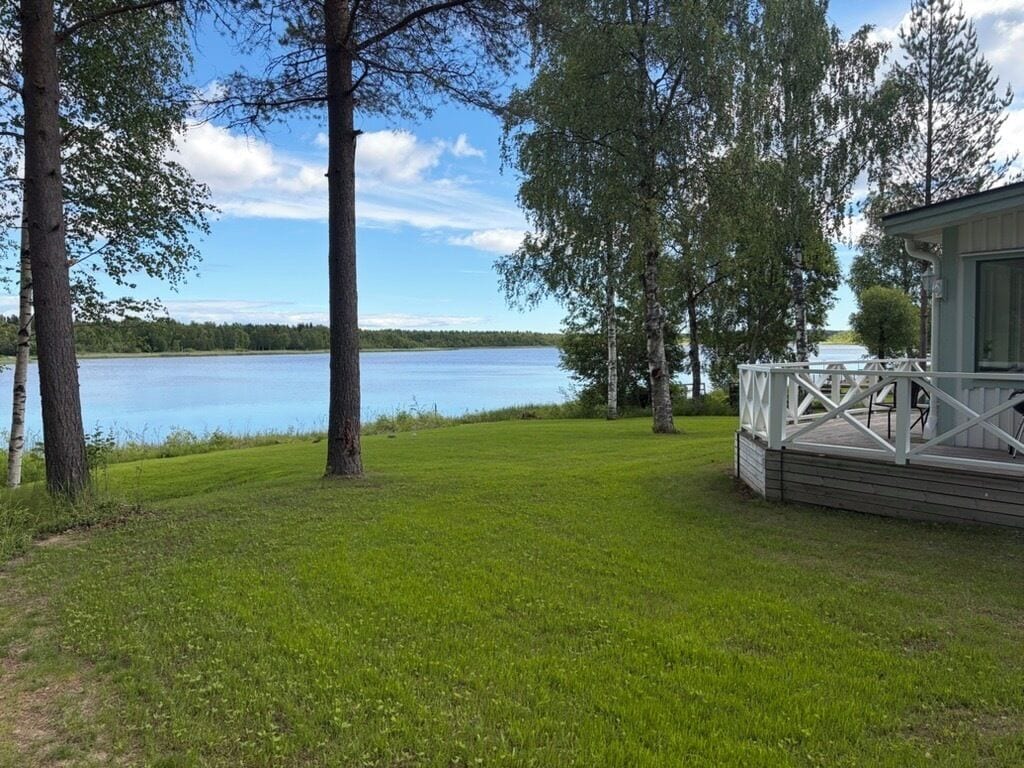 A lakeside property with a grassy lawn, trees, and a cabin with a deck.