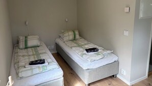 Un petit logement composé d’une seule pièce, comprenant deux lits simples, une table de chevet et une prise électrique au mur.
