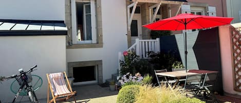 A courtyard with a bicycle, a striped beach chair, a red umbrella, and a table with chairs.
