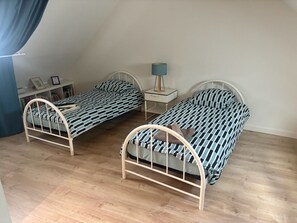 A bedroom with two metal-framed beds, a bedside table with a lamp, and a shelf with books and framed pictures. - Charming 3-bedroom house in Quimper perfect for relaxing stays (Quimper)