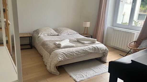 Une chambre à coucher avec un lit, une table de chevet, une lampe et une vue sur l’extérieur.