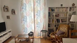 Un salon comprenant un canapé, une table basse, une bibliothèque, un téléviseur et un rideau à motifs.