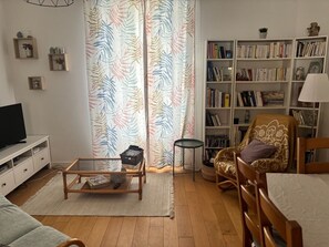 A living room with a sofa, a coffee table, a bookshelf, a television, and a patterned curtain. - Charming 3-bedroom house in Quimper perfect for relaxing stays (Quimper)
