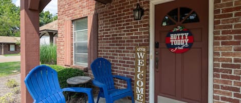 Un bâtiment en briques avec une porte marron, deux chaises bleues et une pancarte indiquant « Bienvenue ».