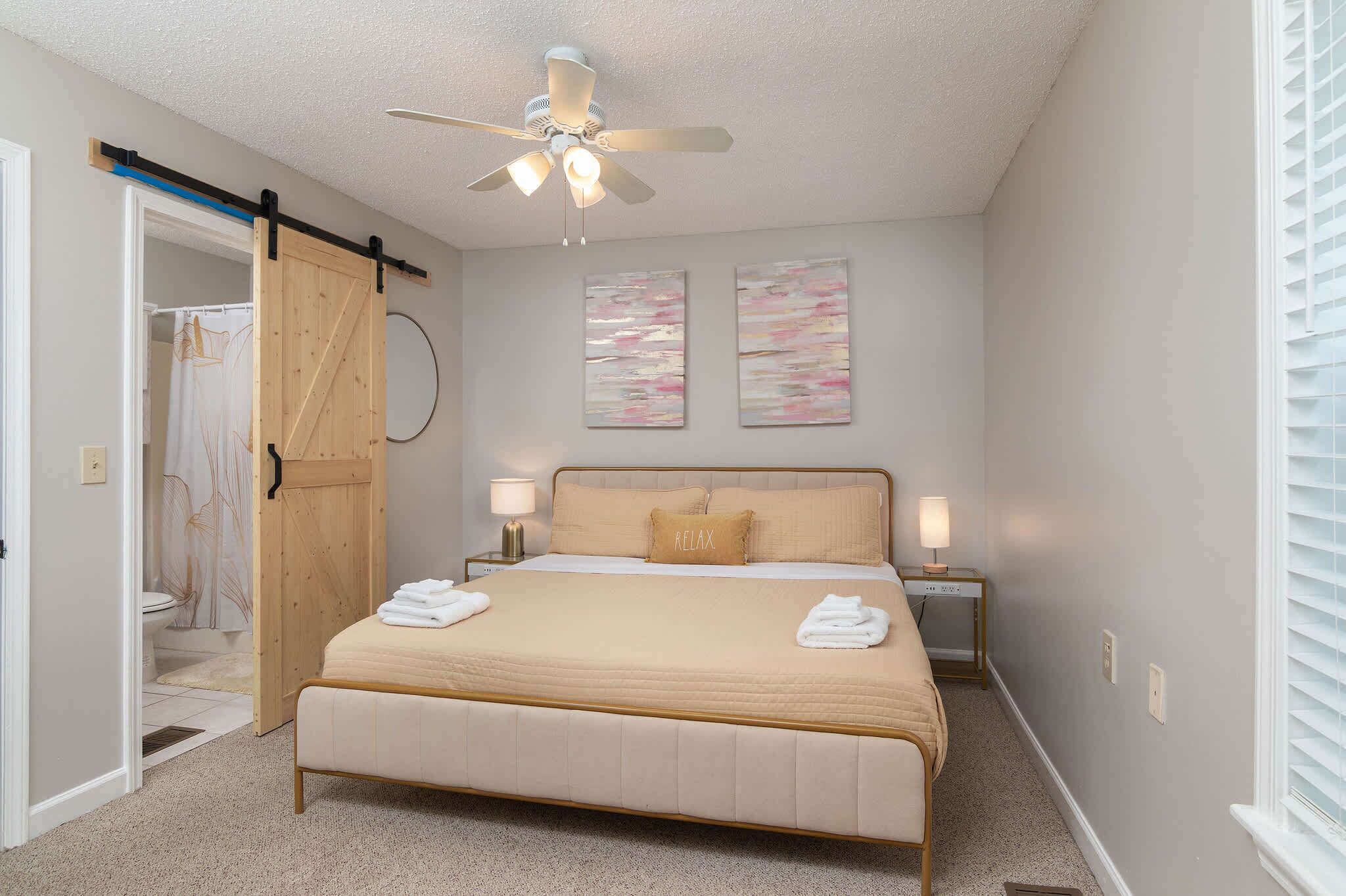 A bedroom with a bed, two bedside lamps, a ceiling fan, a wooden door, and a shower curtain.