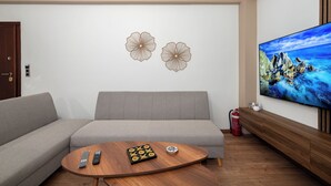 A modern living room with a grey sofa, a wooden coffee table with remote controls, and a large TV displaying a scenic landscape. - Modern Kallithea flat - Metro-AC-WiFI (Kallithea)