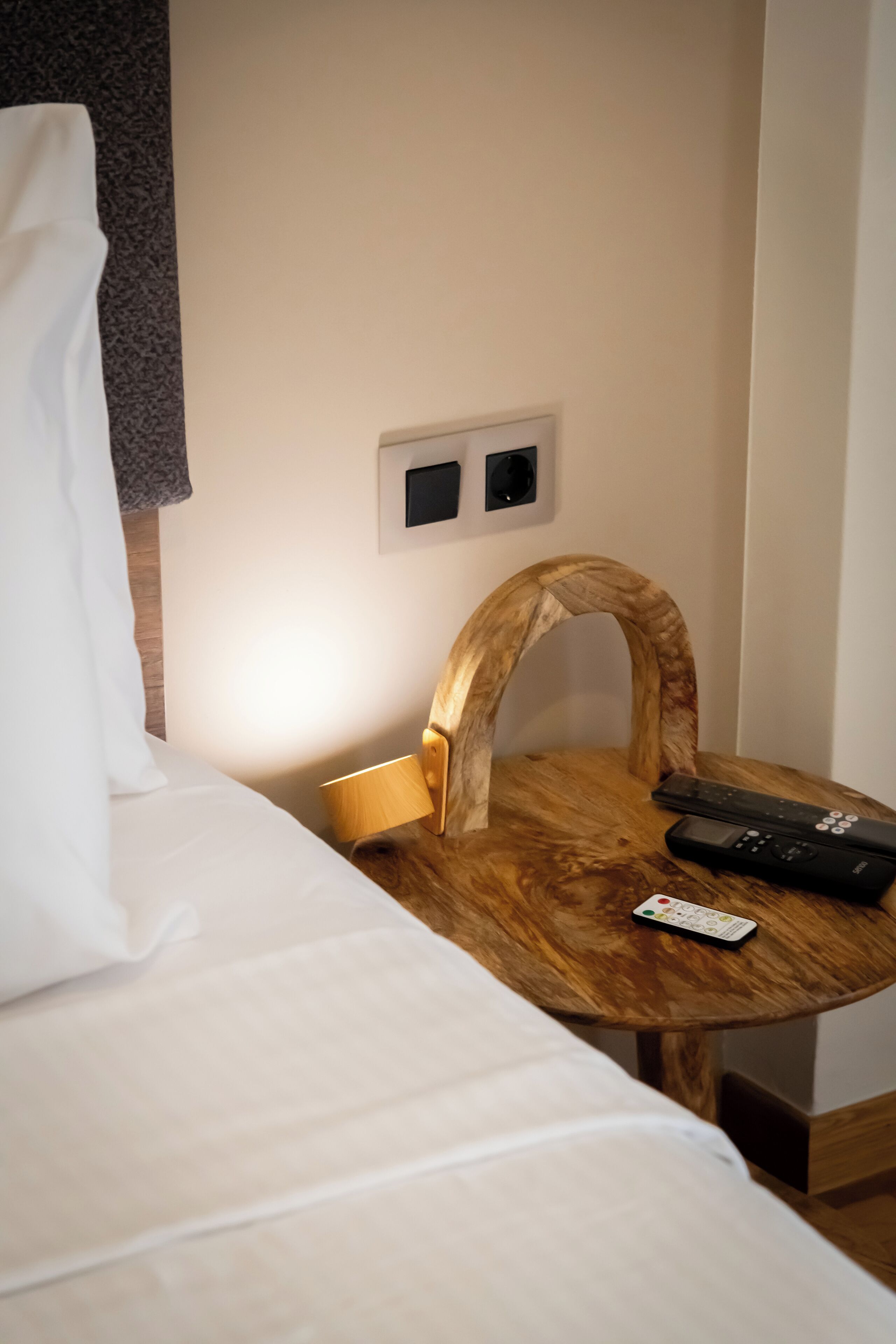 A hotel room with a bed, a small wooden table, and a remote control on the table.