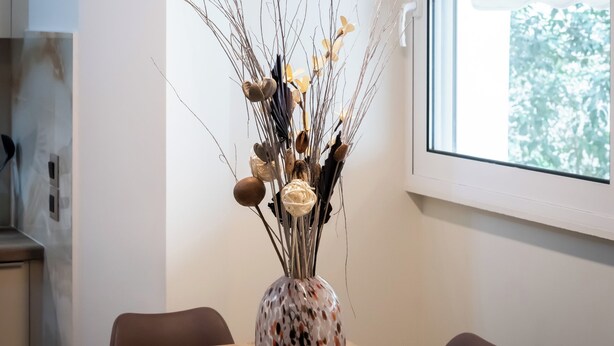 A dining area with a table, chairs, a vase with dried plants, a hanging light fixture, and a window with blinds. - Modern Kallithea flat - Metro-AC-WiFI (Kallithea)