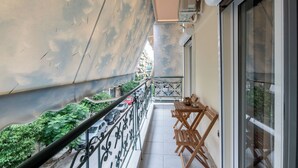 A balcony with a metal railing, a table with chairs, and a view of the street below. - Modern Kallithea flat - Metro-AC-WiFI (Kallithea)