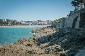 A coastal view with a rocky shoreline, a stone bridge, and buildings in the background. - Cozy nest for 4, 400 m from the beach (Dinard)