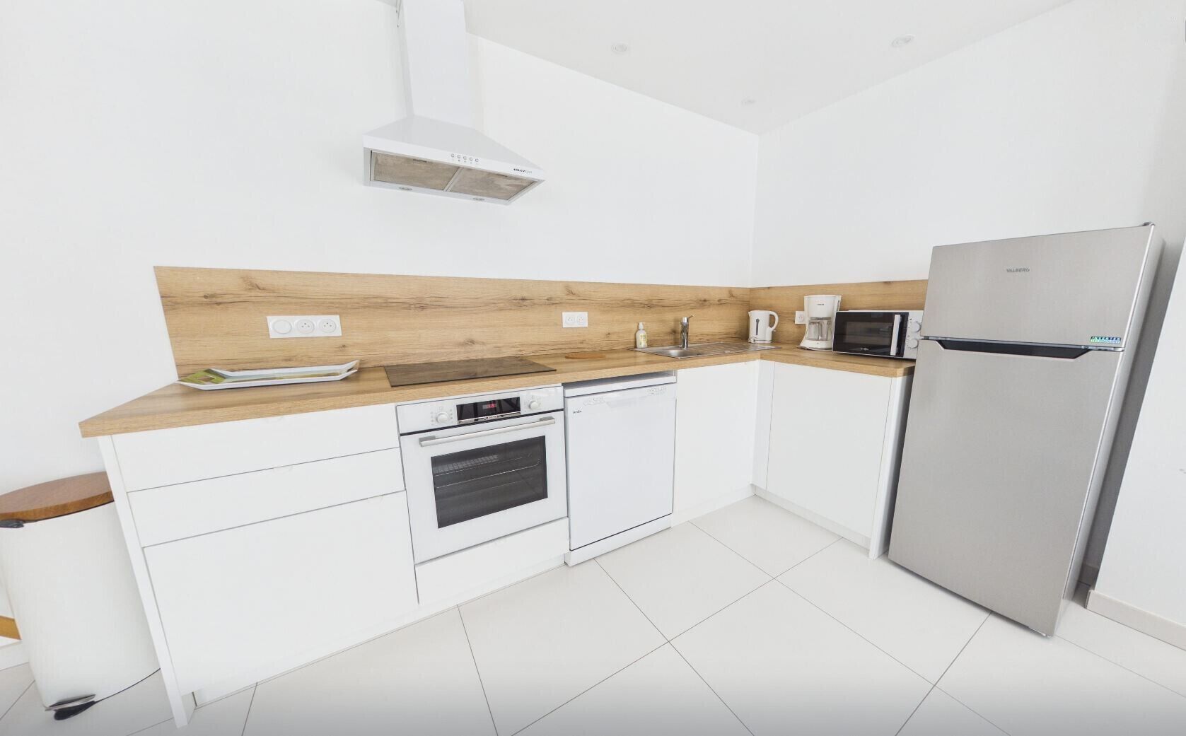 Eine moderne Küche mit weißen Schränken, einer Holzausziehtafel, einem Einbauofen, einer Mikrowelle und einem Edelstahlkühlschrank.
