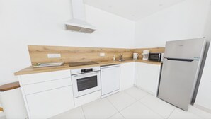 Eine moderne Küche mit weißen Schränken, einer Holzausziehtafel, einem Einbauofen, einer Mikrowelle und einem Edelstahlkühlschrank.