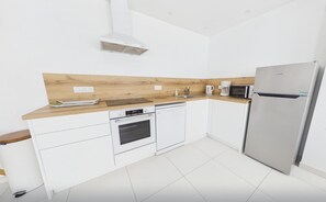 A modern kitchen with white cabinetry, a wooden countertop, a built-in oven, a microwave, and a stainless steel refrigerator. - Cozy nest for 4, 400 m from the beach (Dinard)