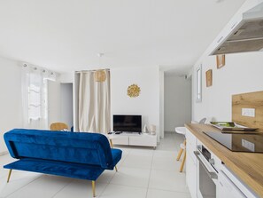 A modern living room with a blue sofa, a TV, and a kitchen area with a wooden countertop. - Cozy nest for 4, 400 m from the beach (Dinard)