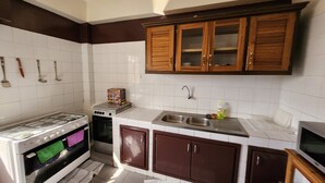 Een keuken met witte en bruine kastjes, een fornuis, een spoelbak en een televisietoestel.