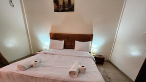 Een opgemaakt bed met witte lakens en twee opgerolde handdoeken, een houten hoofdbord en bedlampen.