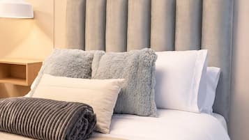A neatly made bed with a grey headboard, a white pillow, and a grey fluffy pillow.