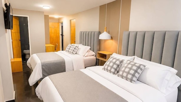 A hotel room with two beds, a TV, a desk, and a bathroom. - Hotel Centro (Cali)