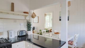 Una cocina con armarios blancos, encimera negra, estufa a gas, tostadora y cafetera.