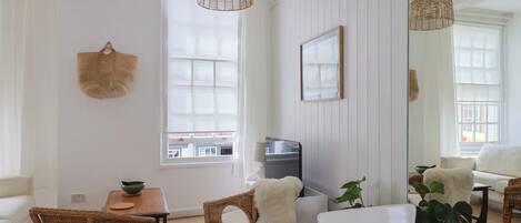 A room with a large window, wicker furniture, a flat-screen TV, and a mirror reflecting the room.