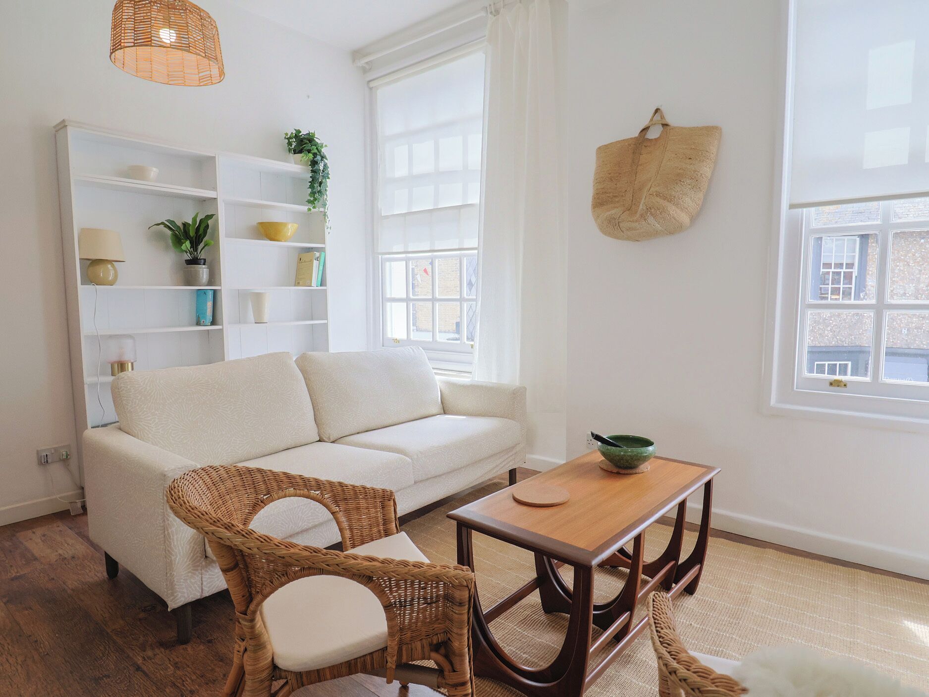 Una sala de estar con un sofá, dos sillones de mimbre, una mesa de madera y una estantería.