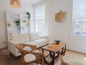 Una sala de estar con un sofá, dos sillones de mimbre, una mesa de madera y una estantería.