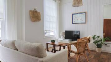 Una sala de estar con un sofá, un televisor, una silla de mimbre y una planta en maceta.