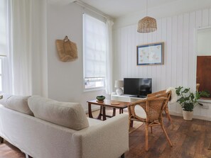 Uma sala de estar com sofá, televisão, cadeira de vime e um vaso de planta.