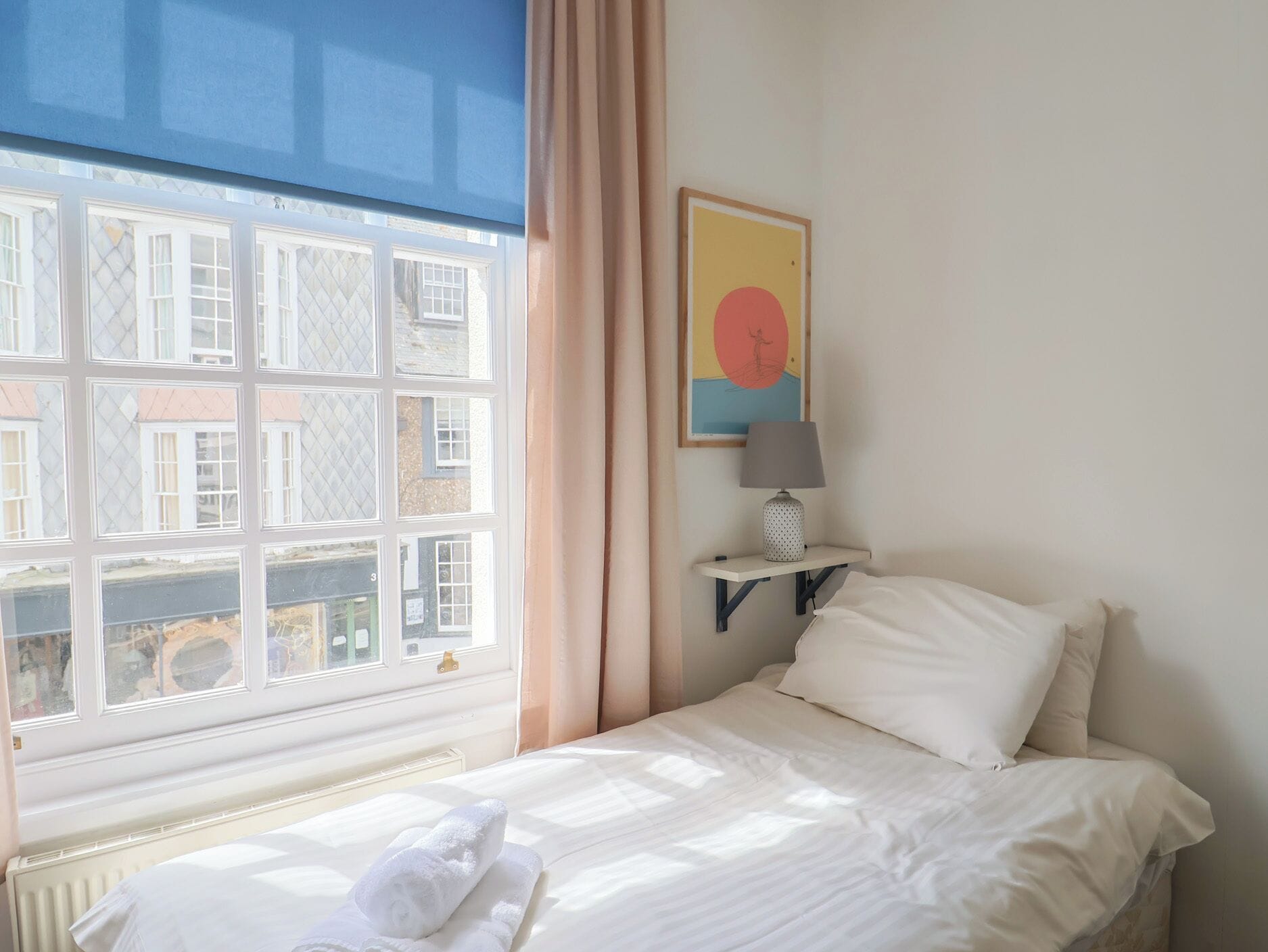 Habitación de hotel con cama, ventana con cortinas, lámpara de pared y un cuadro.