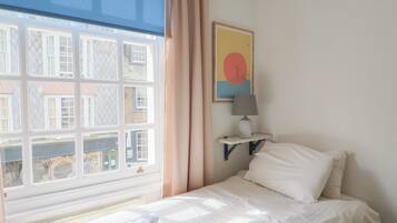 Habitación de hotel con cama, ventana con cortinas, lámpara de pared y un cuadro.