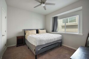 Ein Schlafzimmer mit einem Bett, einem Deckenventilator, einem Fenster mit Jalousien und einem Nachttisch.