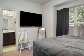Ein Schlafzimmer mit einem Bett, einem Sessel, einem Schminktisch mit Spiegel und einem an der Wand befestigten Fernseher.