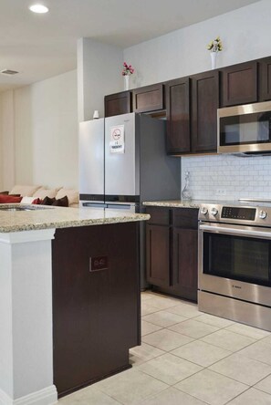 A modern kitchen with dark wooden cabinets, stainless steel appliances, and a granite countertop. - Modern 2BR Haven near Austin & Tesla (Manor)