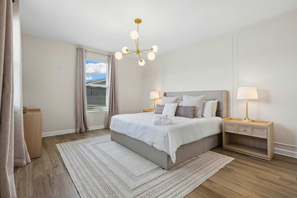 Een moderne slaapkamer met een groot bed, nachtkastjes, een kroonluchter en uitzicht door het raam.