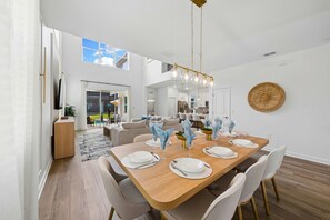 A modern dining area with a wooden table set for six, surrounded by chairs. - Brand New 5BR 5BA Villa w Pool  Spa   Game Room 7800 (Kissimmee)
