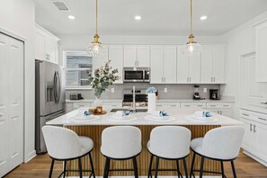 A modern kitchen with white cabinetry, stainless steel appliances, and a central island with bar stools. - Brand New 5BR 5BA Villa w Pool  Spa   Game Room 7800 (Kissimmee)
