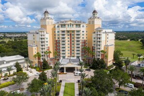 Een meerlaags hotel met een centrale ingang, balkons en een aangelegde omgeving.