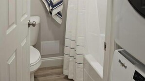 A bathroom with a toilet, a shower curtain, and a washing machine.