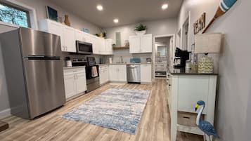 Una cucina moderna con elettrodomestici in acciaio inossidabile, mobili bianchi e un tappeto azzurro con motivi.
